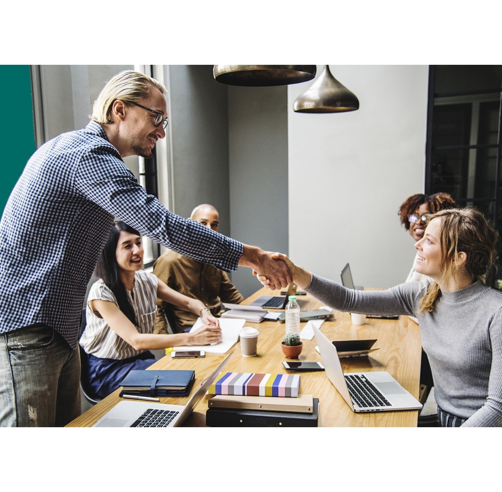 Image of workers sitting around a table chatting and two shaking hands